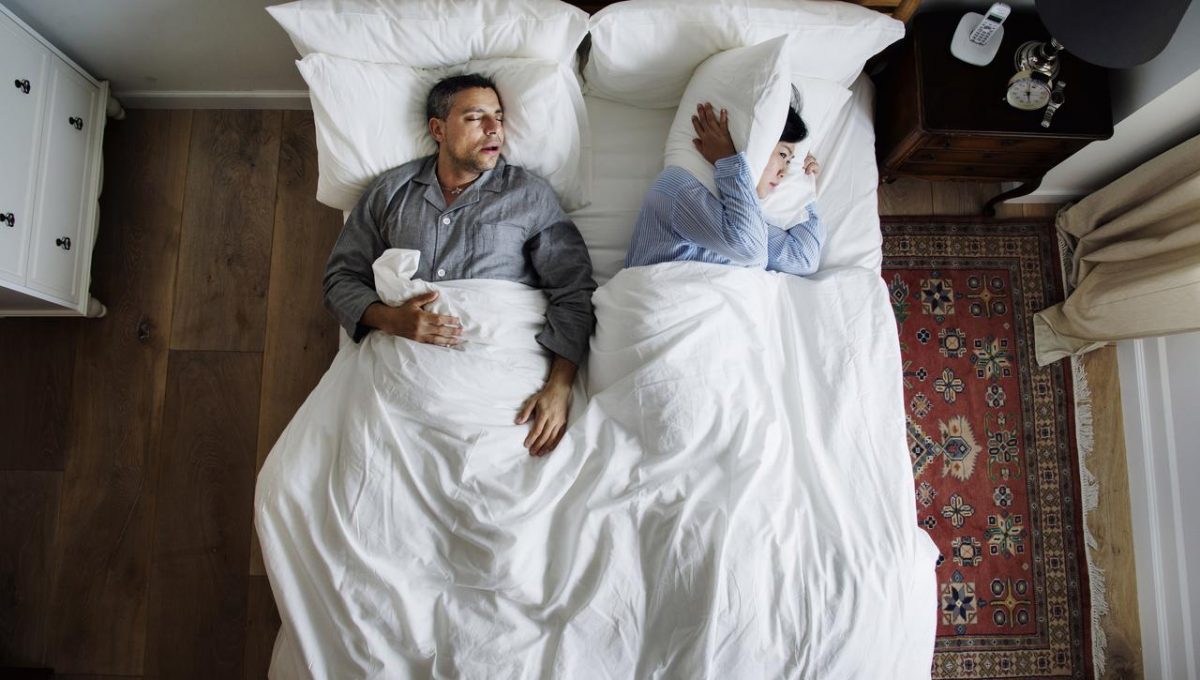 Man snoring and woman holding pillow to hear ears 2