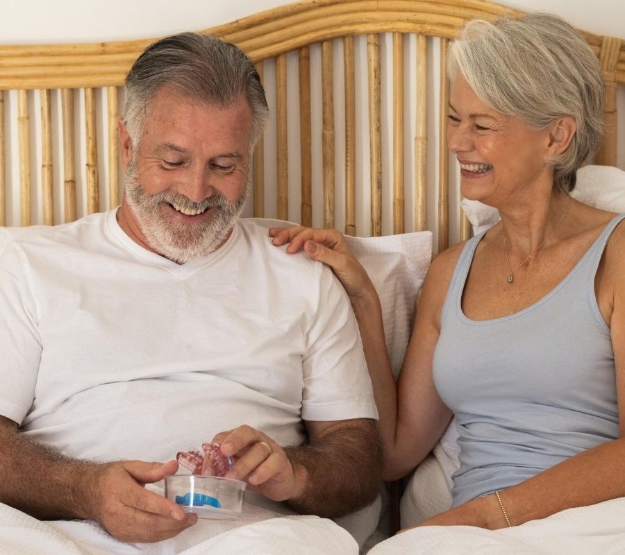 Happy couple in bed smiling at SomnoMed oral device