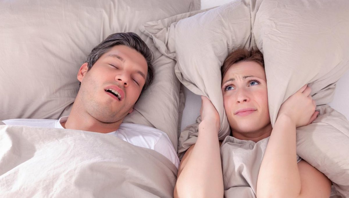 Man snoring and wife holding pillow to ears