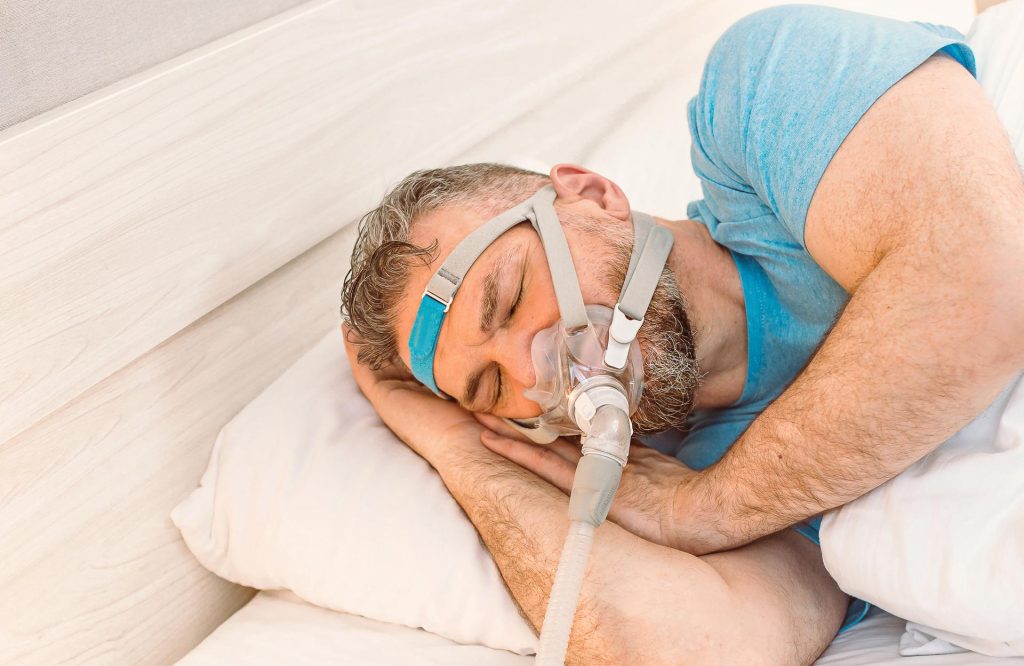 Man lying in bed wearing a CPAP machine
