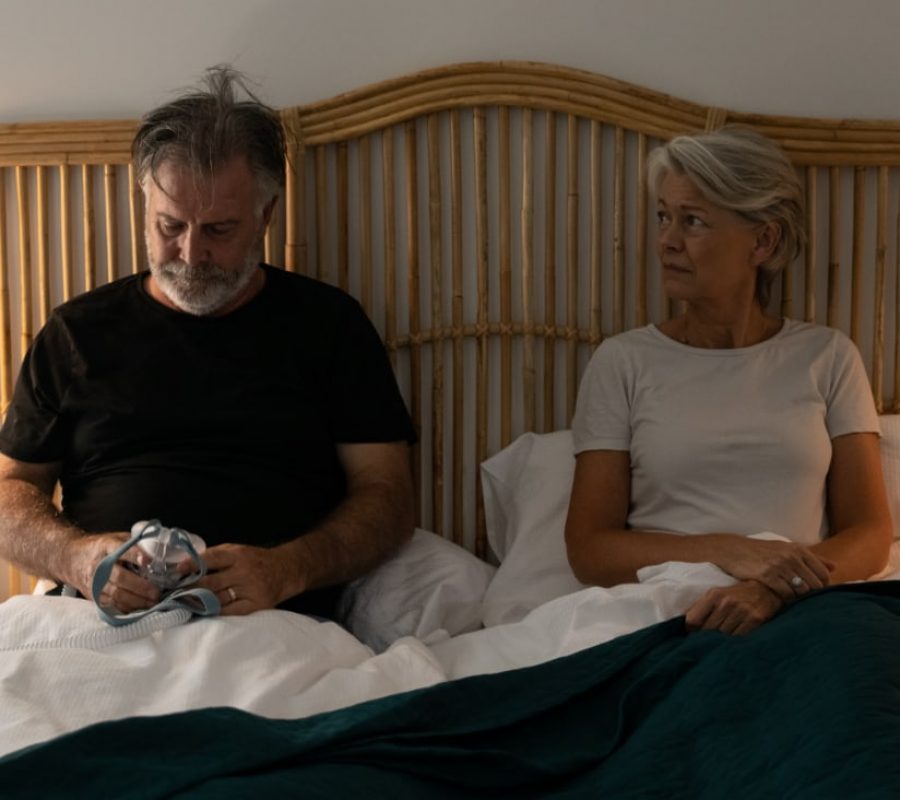 Een koppel in bed, met een CPAP-apparaat in zijn handen.